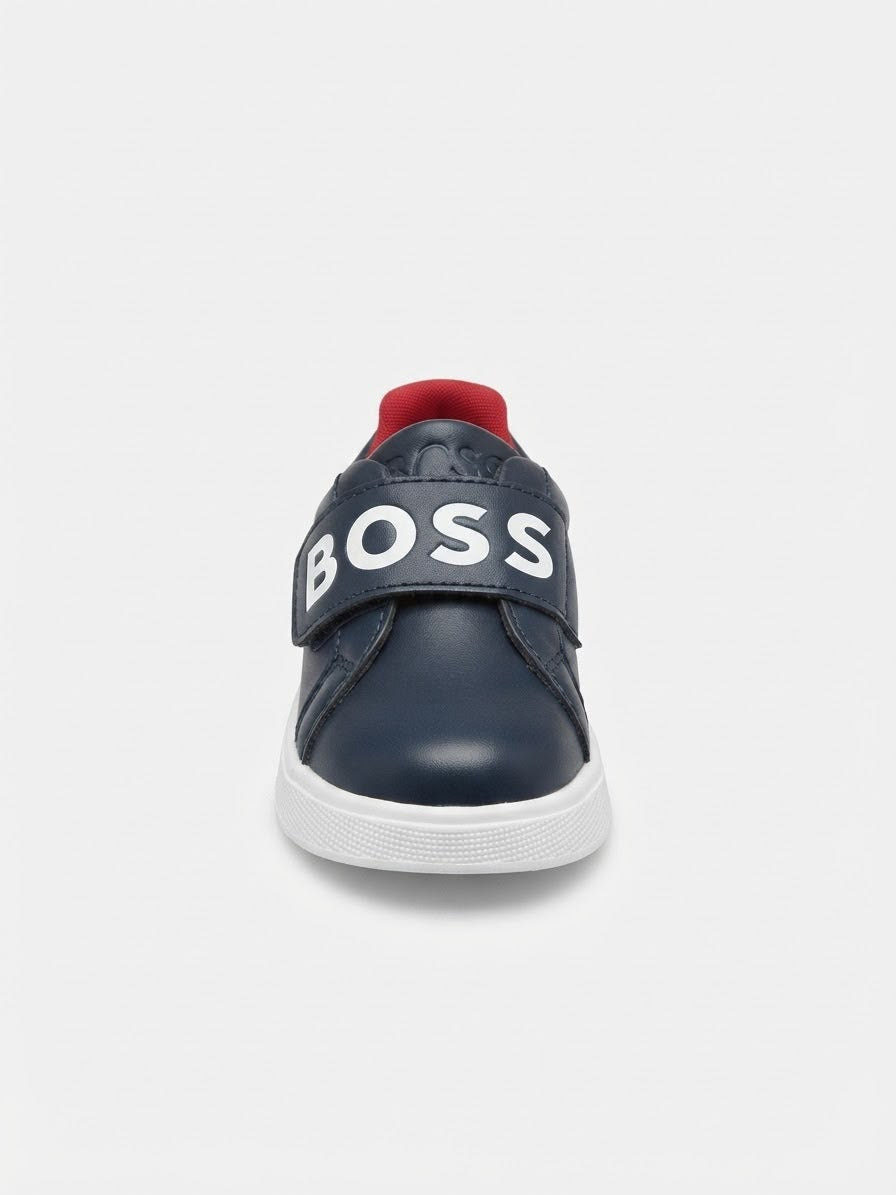 A navy blue low-top sneaker with a white witing on strap and a white rubber sole, shown from the back on a light gray background.