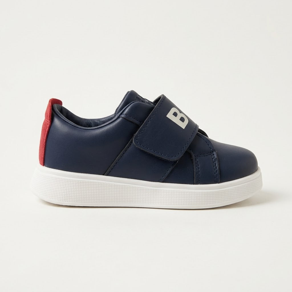 A navy blue children's low-top sneaker with a white sole, featuring a hook-and-loop strap and a red heel tab.