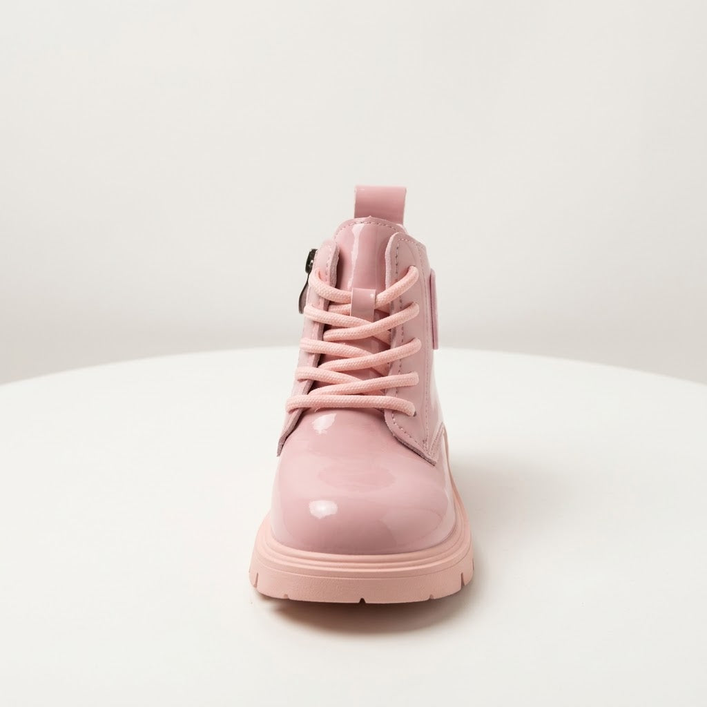 A single light pink patent leather lace-up ankle boot with a matching pull tab and thick sole, photographed from the front on a white circular platform against a light gray background.