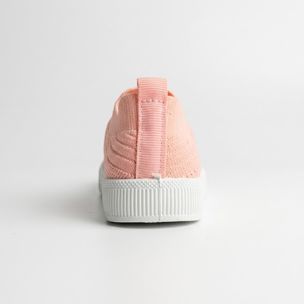 A single knit slip-on sneaker shown from the back, featuring a light peach-pink knit upper with a matching pull tab and a thick white ribbed rubber sole, set against a clean white background.