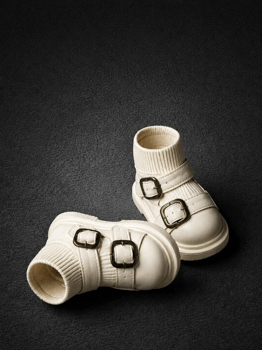A pair of off-white ankle boots with ribbed knit cuffs and double buckle straps, displayed on a dark textured background.